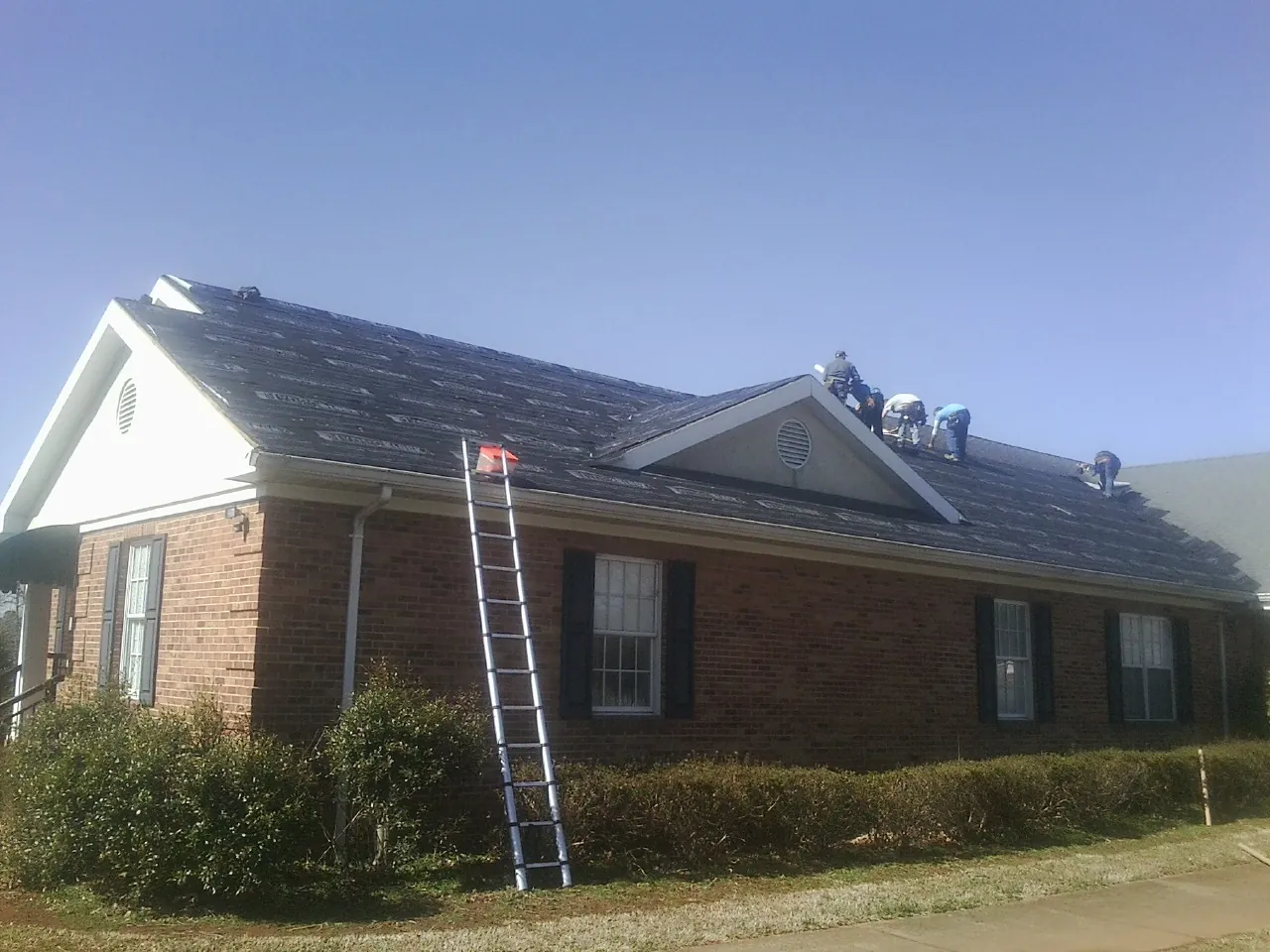 Crew tearing shingles off a brick ranch roof with a ladder set — Metal Roof Repair work by our crew in Hawesville