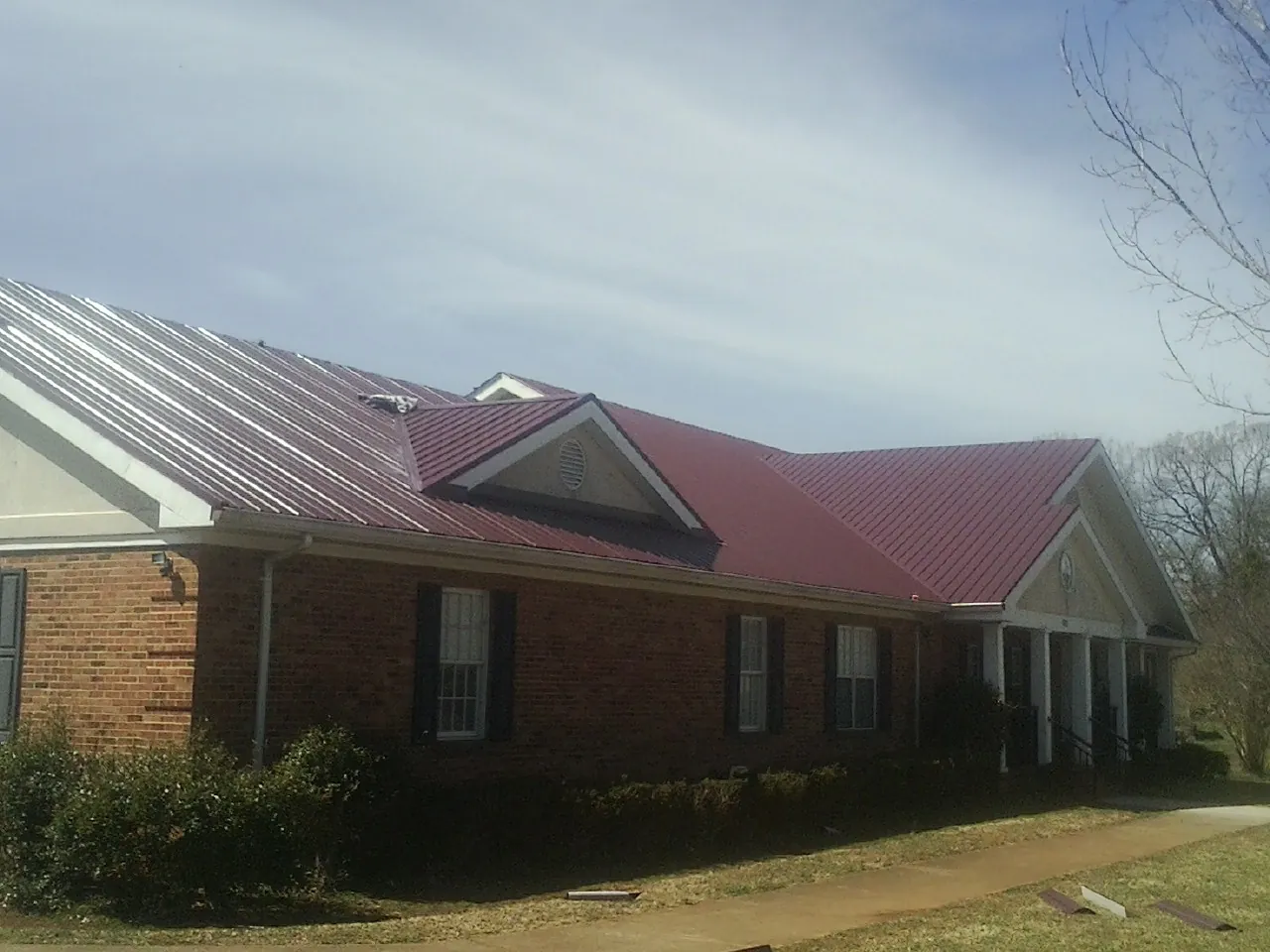 Red metal roof with gabled entries on a long brick building, from a Hail Damage Roof Repair job in Hawesville