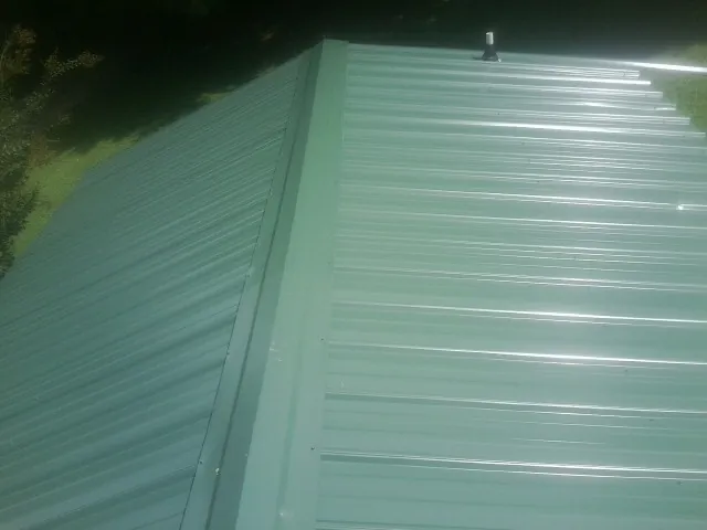 New green metal panels meeting at the ridge of a roof — Flat Roof Repair work by our crew in Hawesville