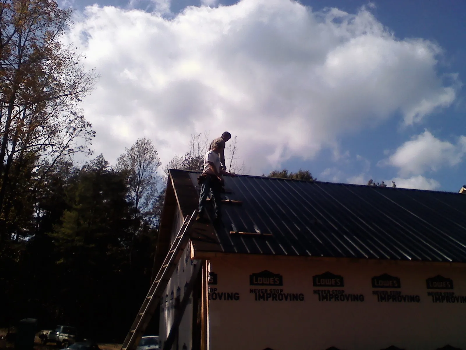 Roofer fastening dark metal panels high against a cloudy sky, from a Roof Inspection job in Hawesville