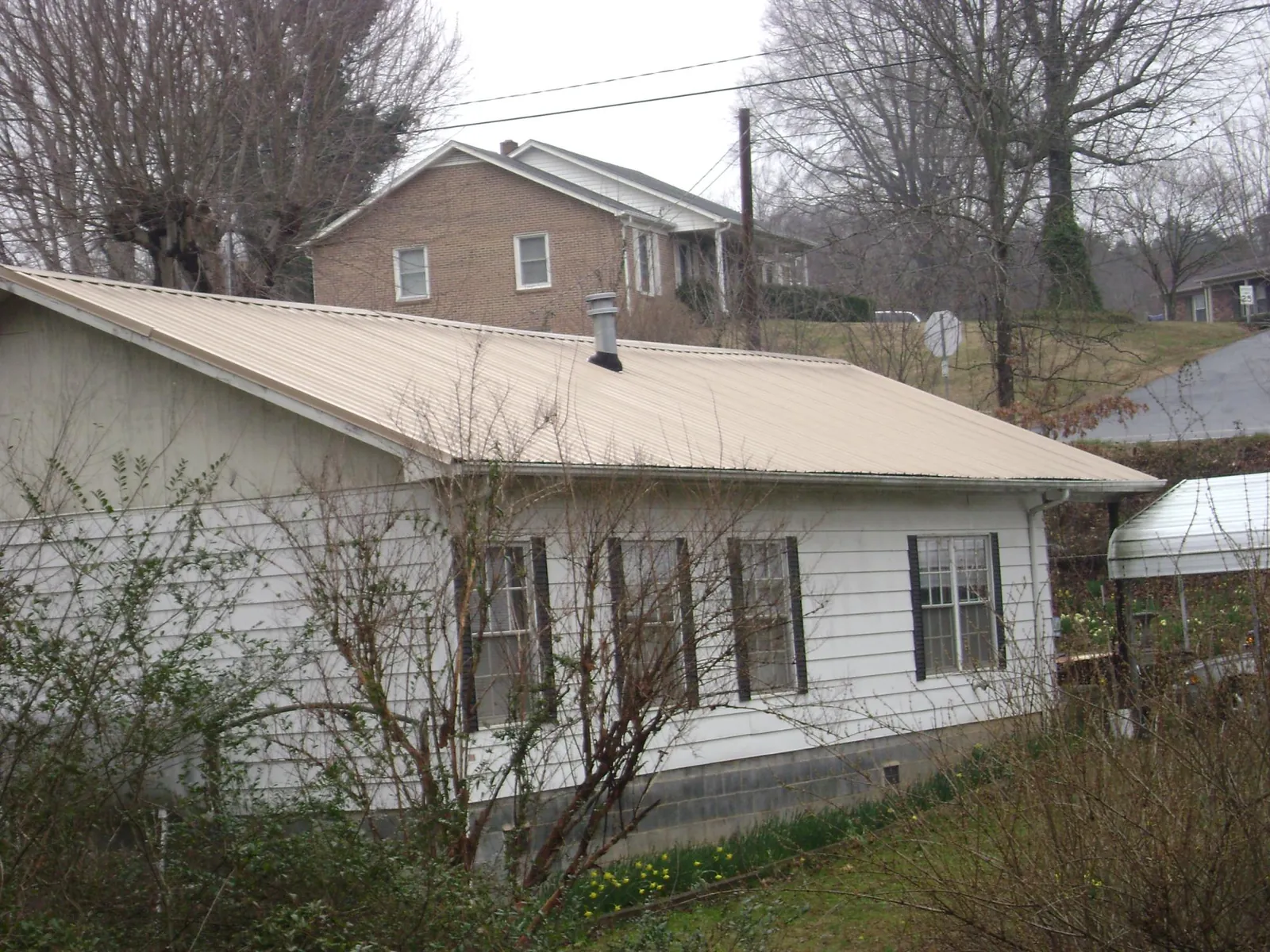 Tan metal roof on a white sided house set into a hillside — Commercial Roofing by Roofing Brothers in Hawesville